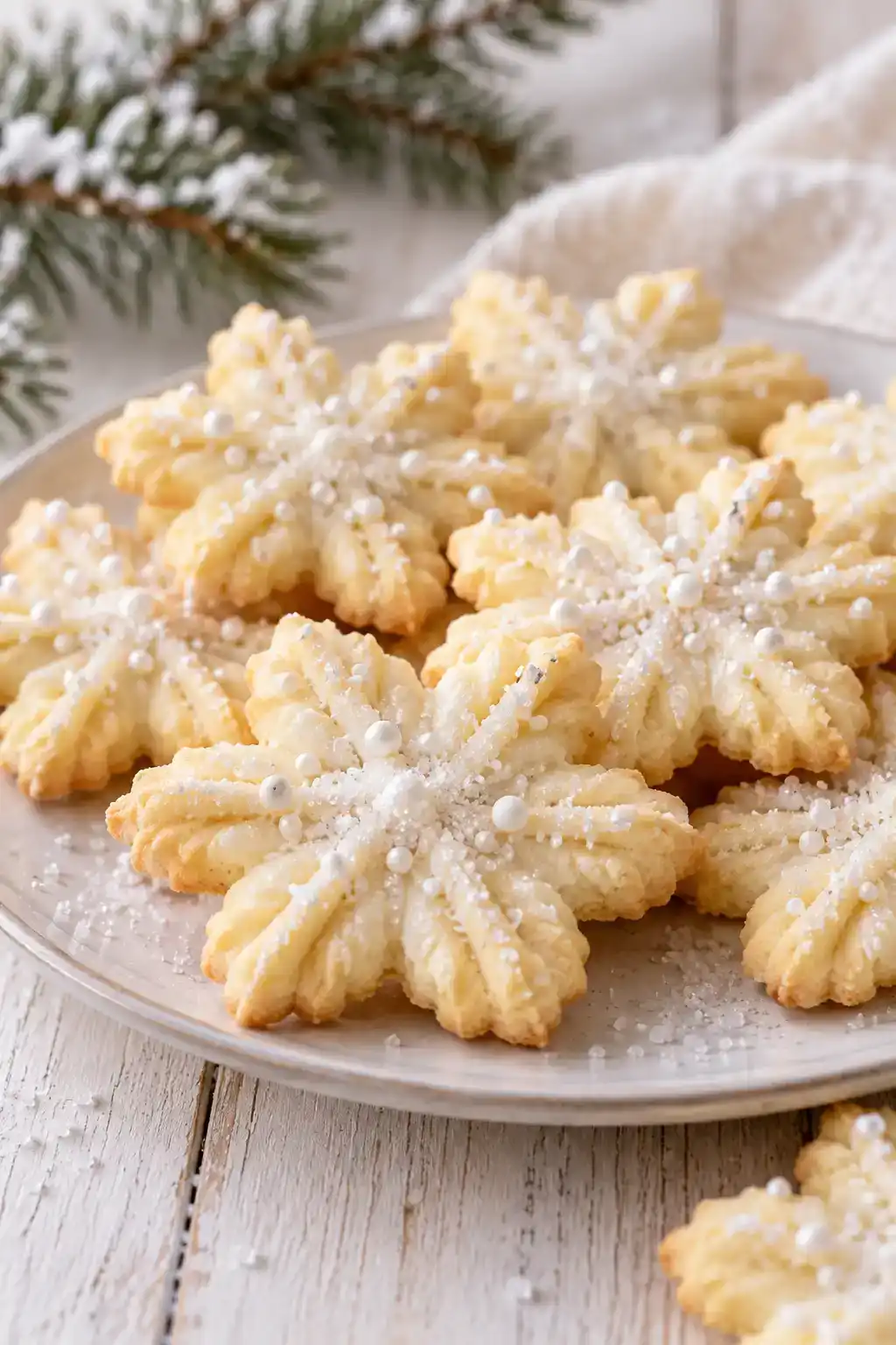 A batch of snowflake spritz cookies arranged on a ceramic plate.